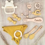 Coffret de naissance jaune comprenant des jouets de stimulation, un bavoir en silicone et des couverts en bois personnalisés.