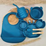 Coffret Naissance en silicone bleu avec un bavoir, assiette en forme de crabe, bol en ours et tasse avec paille.